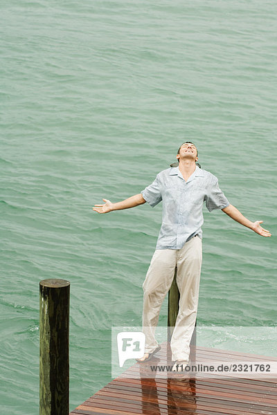 Mann lehnt sich im Regen auf den Pier zurück  Arme ausstrecken  Augen geschlossen  Hochwinkelansicht