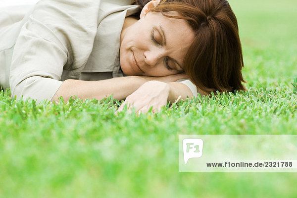 Frau auf Gras liegend mit Kopf auf den Armen liegend  Augen geschlossen