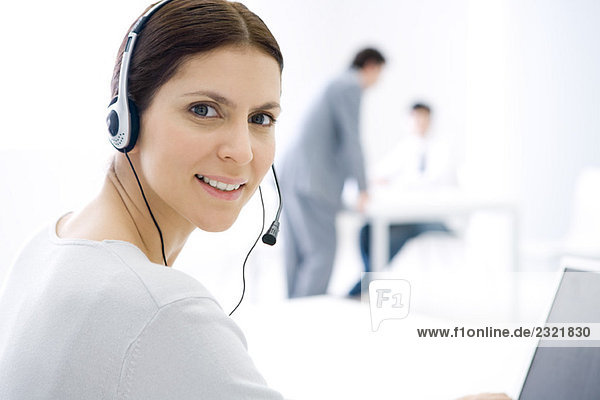 Woman wearing headset  sitting at computer  smiling at camera