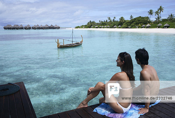 Couple sitting on pier at Coco Palm Dhuni Kolhu Resort in Maldives