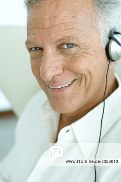 Mature man listening to headphones  smiling at camera  close-up