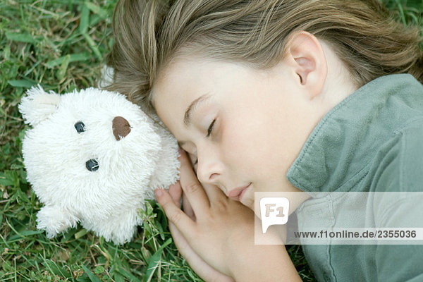 Junge im Gras liegend mit geschlossenen Augen  Kopf auf Teddybär ruhend