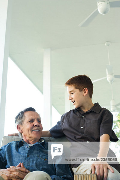 Großvater und Enkel sitzen zusammen auf der Veranda  beide lächelnd.