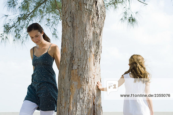 Zwei Schwestern gehen um den Baumstamm herum  kleines Mädchen berührt Baum mit der Hand