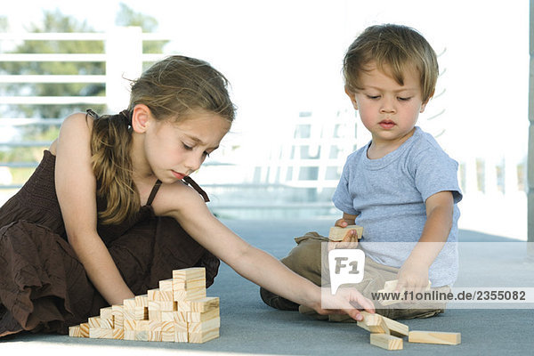 Bruder und Schwester sitzen auf dem Boden und spielen mit Bausteinen zusammen.