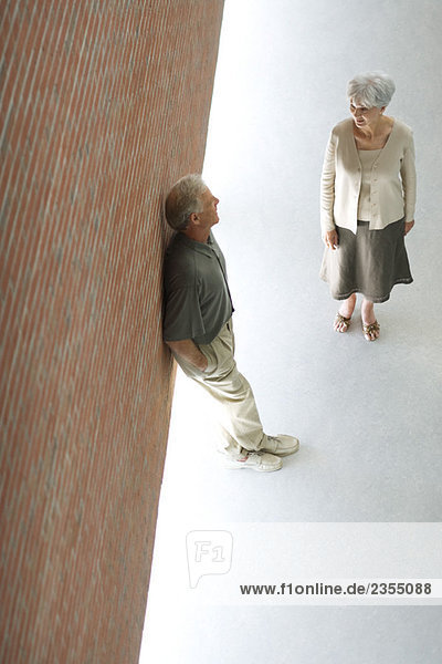 Couple talking together  man leaning against wall with hands in pockets  high angle view