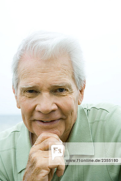 Älterer Mann mit Hand unter dem Kinn  lächelnd vor der Kamera  Porträt