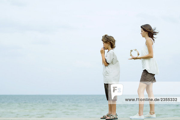 Geschwister stehen am Strand  Junge spielt Mundharmonika  Teenagermädchen spielt Tamburin  Blick auf die Aussicht