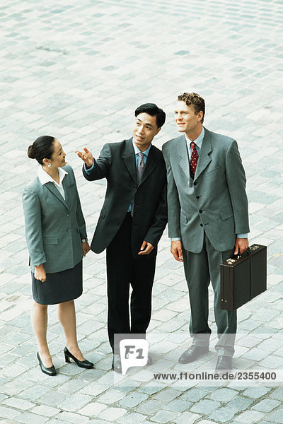 Three professionals standing together outdoors  one gesturing with hand  two looking up  high angle view