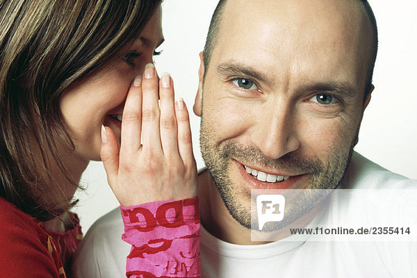 Woman whispering in man's ear  man smiling at camera