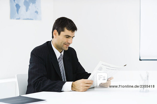 Geschäftsmann am Schreibtisch sitzend  Zeitung lesend  lächelnd