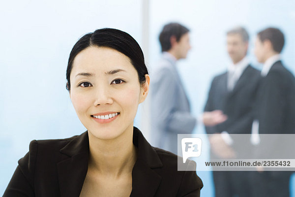 Businesswoman smiling at camera  male colleagues standing in background