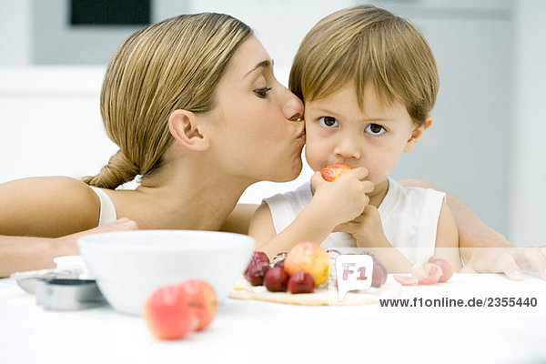 Frau küsst kleinen Jungen auf Wange  Junge isst Apfel