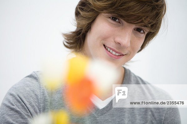 Junger Mann hält Blumen vor der Kamera  lächelnd  Nahaufnahme