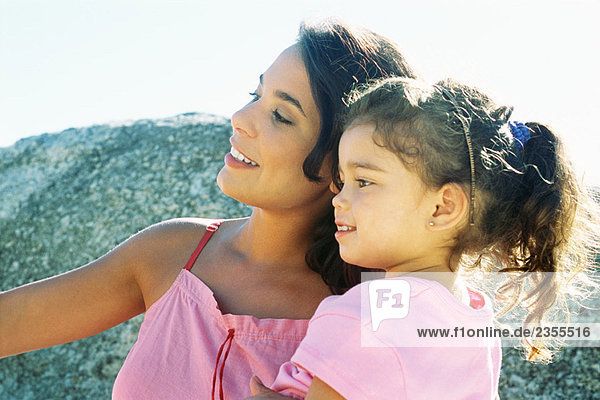 Mother and daughter looking away outdoors  smiling  side view