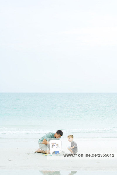Vater und Sohn am Strand  spielen mit dem Sandeimer