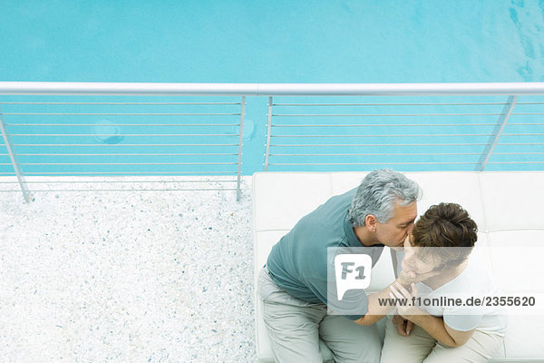 Paar auf dem Balkon sitzend  Mann küsst die Wange der Frau  hoher Blickwinkel