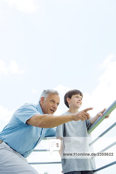 Man standing with arm around grandson's shoulder  pointing  both looking away  low angle view