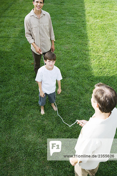 Boy playing jump rope with two men  smiling at camera