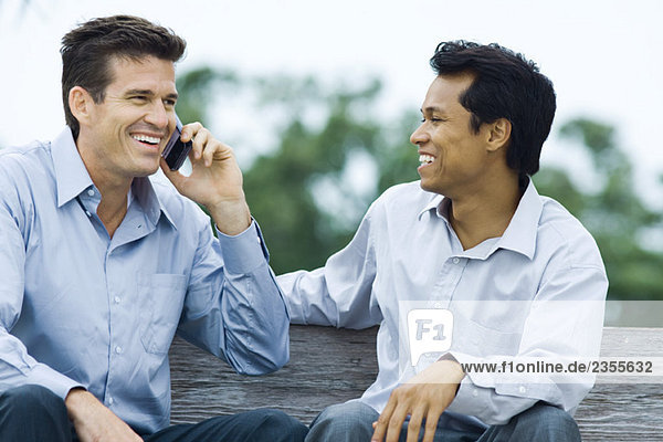 Zwei Männer sitzen auf der Bank  lächelnd  einer mit dem Handy.