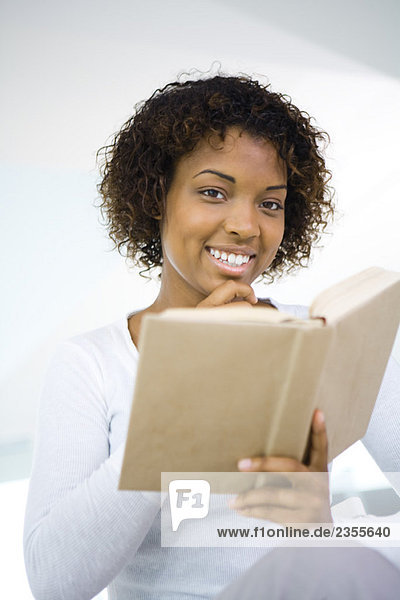 Woman holding book in one hand  other hand under chin  smiling at camera