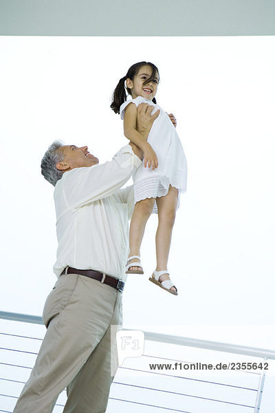 Großvater hält Enkelin in der Luft  beide lächelnd  Blickwinkel niedrig