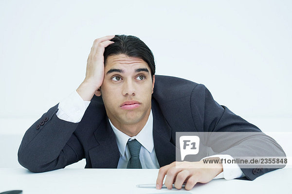 Young businessman slouching on desk  holding head