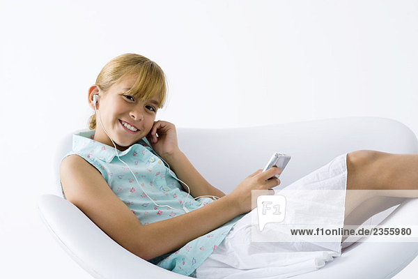 Preteen girl sitting in chair  listening to MP3 player  smiling at camera