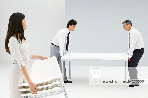 Professionals setting up office  men moving table  woman carrying chairs