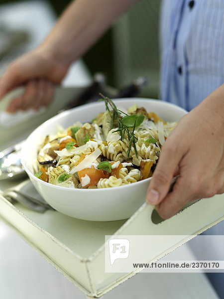 Mid section view of woman holding bowl of pasta salad on tray