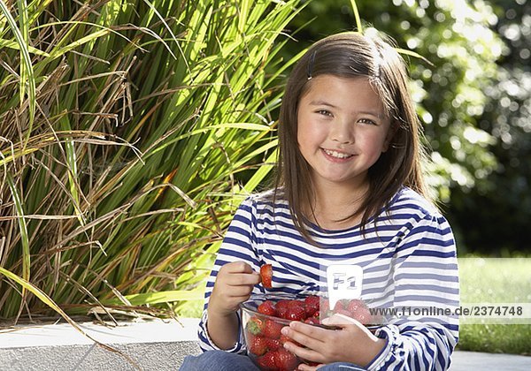 Young girl sitting outdoors with a bowl of strawberries smiling