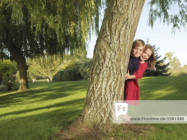Junge und Mädchen  die sich hinter einem Baum verstecken.