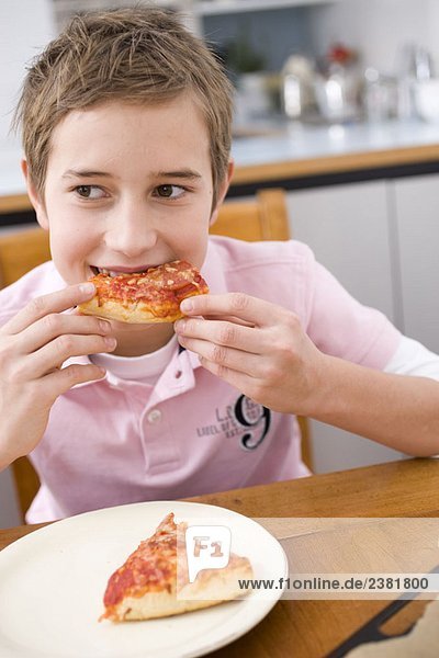 Junge  der ein Stück Pizza isst.