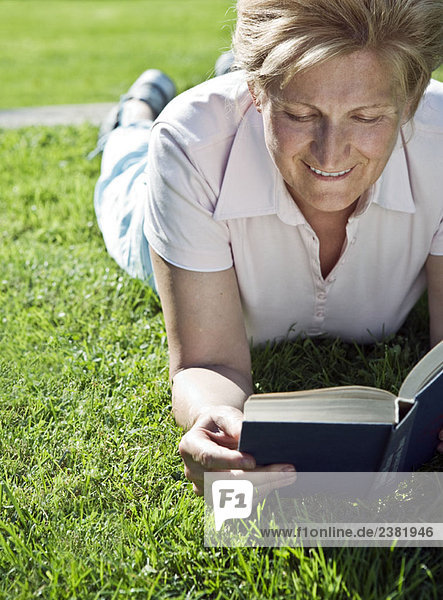 Frau auf Gras liegend lesend