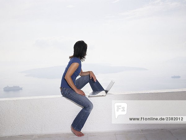 Woman with laptop sitting on a low wall