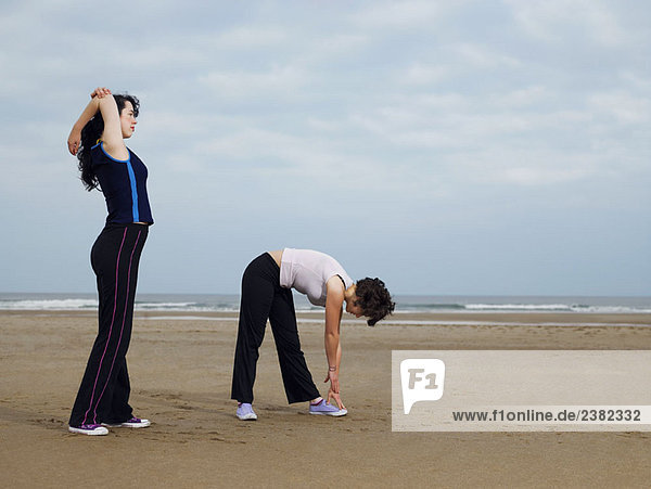 Two young females stretching on beach