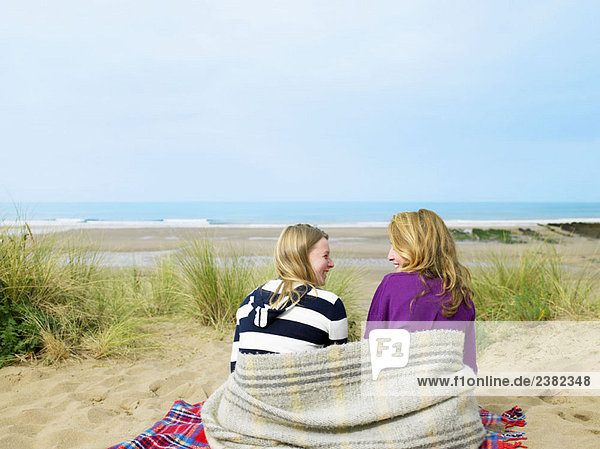 Girls sitting on sand dune with blanket