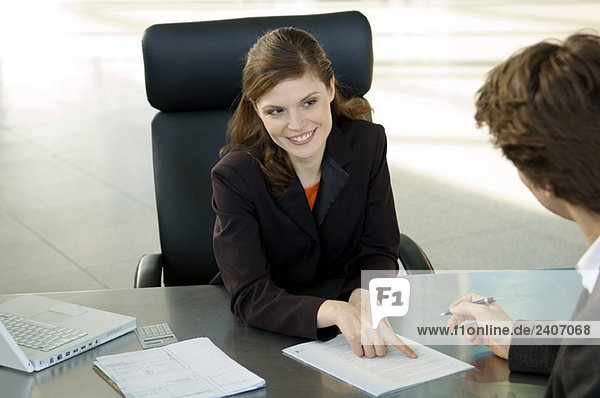 Geschäftsfrau  die auf einen Vertrag zeigt und Geschäftsmann  der vor ihr sitzt.