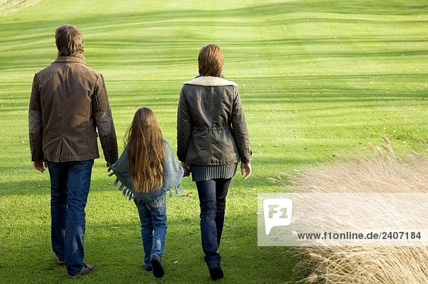 Rückansicht eines Mädchens  das mit seinen Eltern in einem Park spazieren geht.