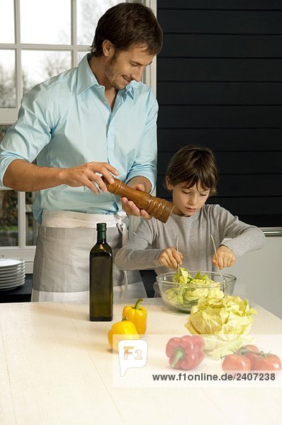 Mittlerer Erwachsener  der mit seinem Sohn in der Küche das Essen zubereitet.