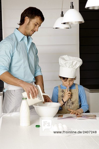 Mid adult man making a cake with his son in the kitchen