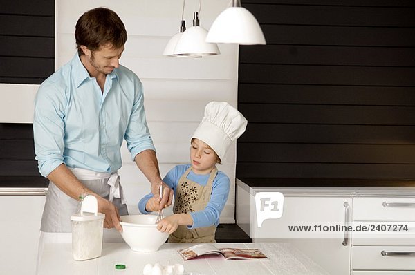 Ein erwachsener Mann  der mit seinem Sohn in der Küche einen Kuchen backt.