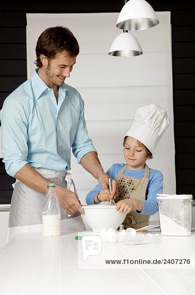 Ein erwachsener Mann  der mit seinem Sohn in der Küche einen Kuchen backt.