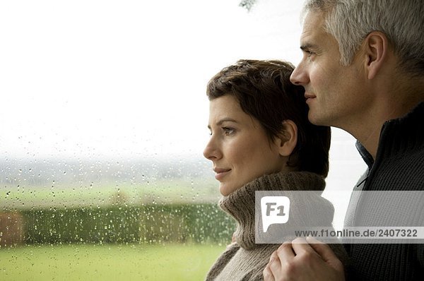 Mature man and a mid adult woman looking out through a window