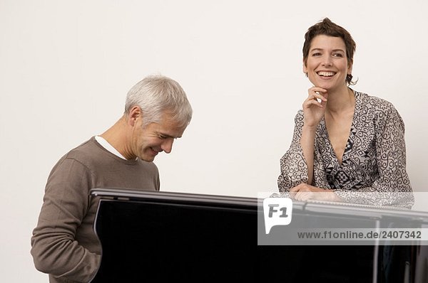 Ein reifer Mann  der Klavier spielt  und eine erwachsene Frau  die in seiner Nähe steht.