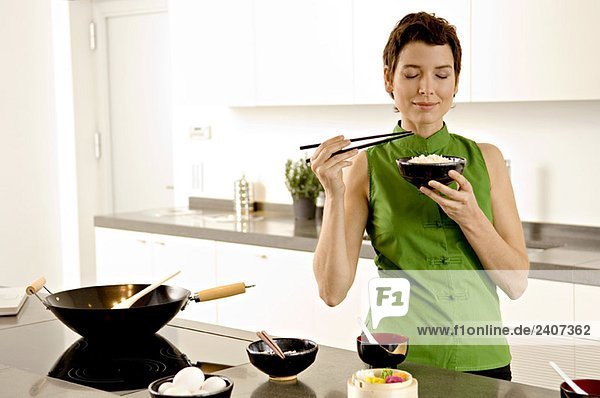 Mittlere erwachsene Frau  die eine Schüssel Reis in der Küche riecht.