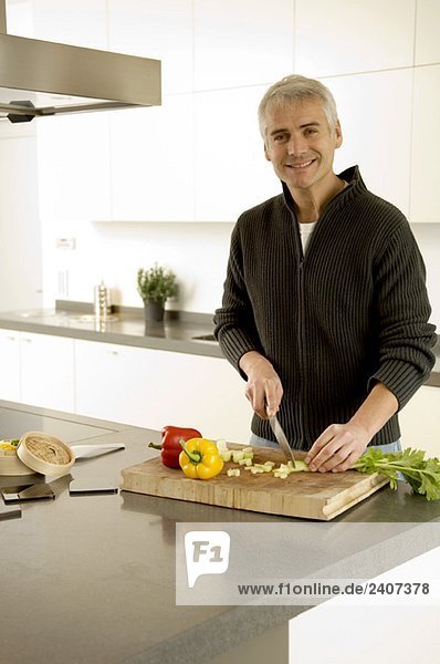 Porträt eines reifen Mannes  der in der Küche Gemüse hackt.