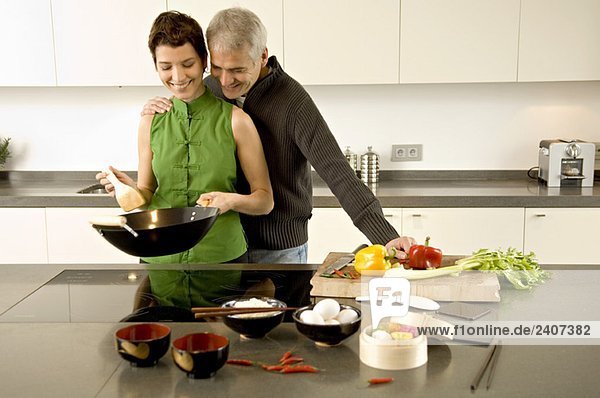 Mittlere erwachsene Frau bei der Zubereitung des Essens mit einem reifen Mann  der mit einem Arm um sie herum in der Küche steht.
