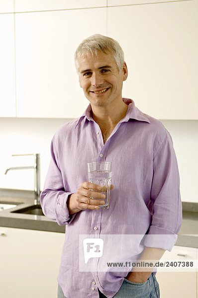 Porträt eines reifen Mannes mit einem Glas Wasser in der Küche
