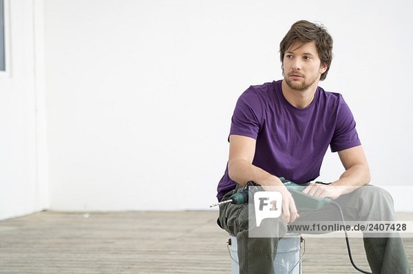Mid adult man holding a drill and sitting on a paint can